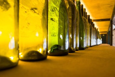 Rafta bir sürü boş cam şişeler var. Kafede dekorasyon var. Kürsüde lambayla aydınlatılmış farklı şişeler