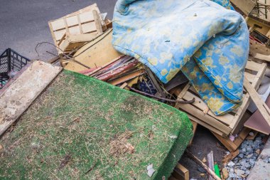 Büyük bir odun, karton, plastik sandık ve eski döşek yığını bir çöp yığınının üzerinde. Tahta, plastik ve karton kutular. Çileklerin altındaki çöp yığını.