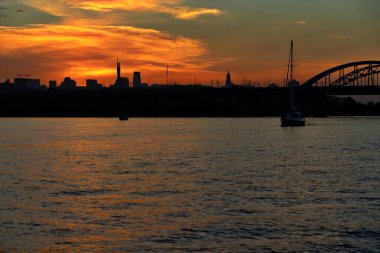 Gün batımında gökdelenler, tarihi anıtlar ve Dinyeper nehrinin üzerindeki renkli gökyüzü ile Kyiv silueti panoraması. Gemiler gün batımında şehrin arka planına karşı nehirde yelken açarlar.