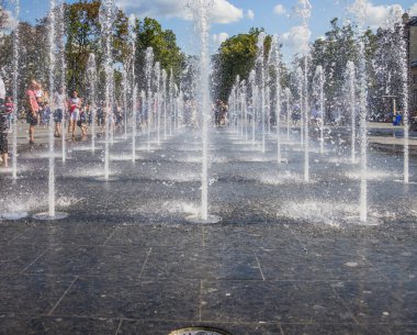 Ukrayna. LVIV - 07 Ağustos 2021. Küçük mutlu çocuklar sıcak günlerde açık havuzda eğlenirler. Gençler ve çocuklar şehir çeşmelerinin arasında koşuyorlar.