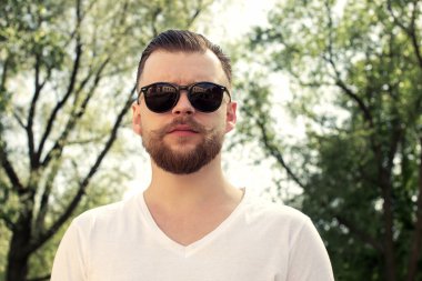 Genç adam bir sakal ve bıyık güneş gözlüğü ve beyaz t-