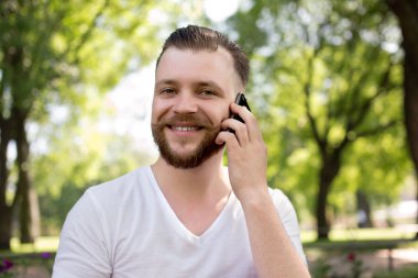 Kameraya gülümseyen ve akıllı telefonda konuşurken mutlu hipster adam