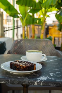 Bir fincan kibrit yeşil çay ve kahve dükkanının açık terasındaki ahşap masanın üzerinde mermer bir kek. Tatlıyla kahvaltı.