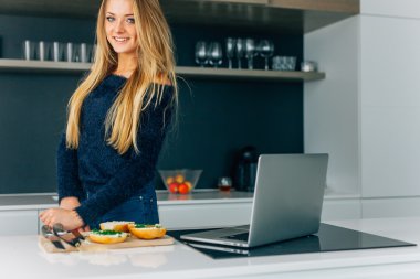 Genç kız mutfakta sandviçler. Kitch üstünde laptop