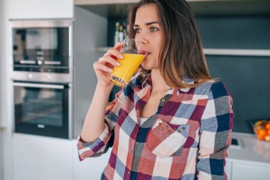 Güzel genç kadın mutfakta portakal suyu içme. 