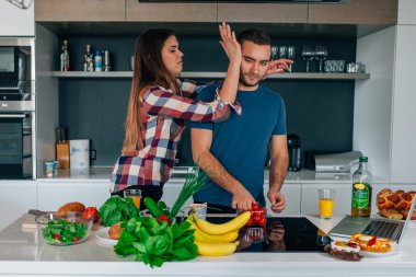Genç çift mutfakta yemek hazırlanıyor. Kız onu silinerek 