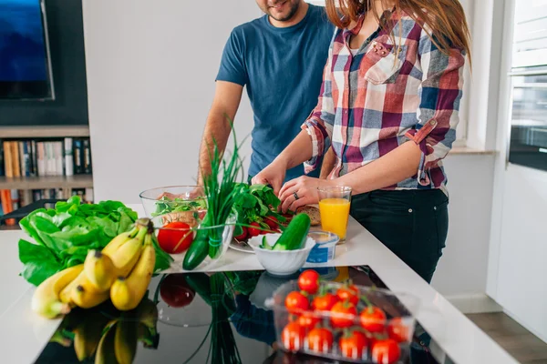 Young couple is preparing dinner. Girl is cutting food. Man is h — Stock Photo, Image
