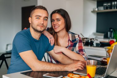 Genç kithcen içinde oturan ve dizüstü bilgisayar kullanarak çift. S olduklarını