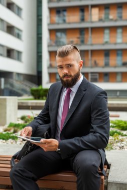Genç bir bankta oturan ve tablet PC'yi kullanma işadamı sakallı