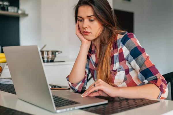 Chica triste sentado i la cocina y el uso de la computadora portátil . — Foto de Stock