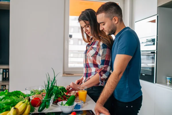 Una pareja joven está preparando la cena. La chica está cortando comida. El hombre es h — Foto de Stock