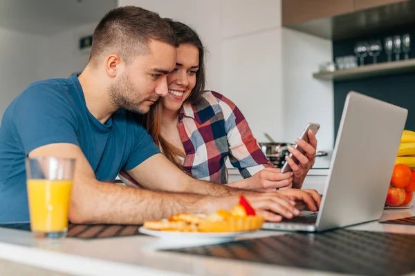 Junges Paar in der Küche. Mann benutzt Laptop. Mädchen i — Stockfoto