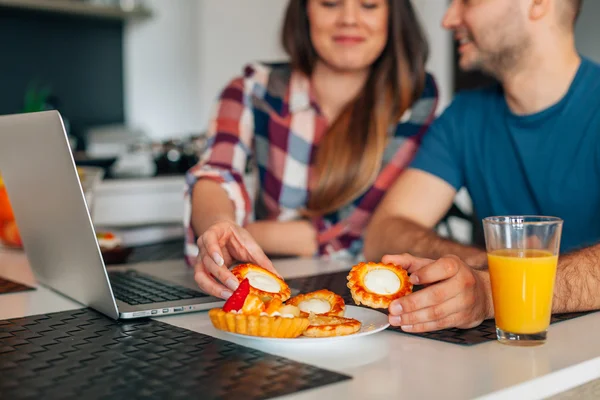 Pareja joven sentada en la cocina y degustando capcakes con fr — Foto de Stock