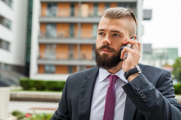 Joven hombre de negocios barbudo usando teléfono móvil fuera de la oficina . — Foto de Stock