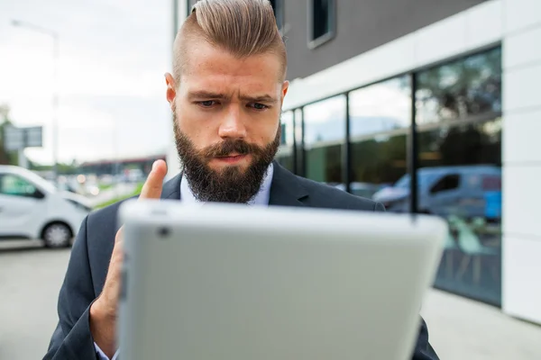 Jonge, bebaarde zakenman met zijn tablet-pc. Hij is verbaasd. — Stockfoto