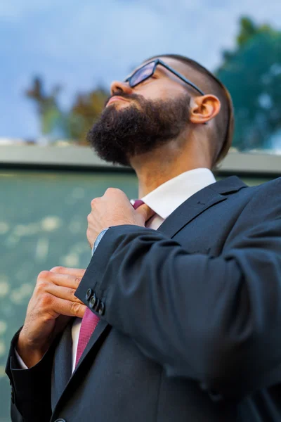 Young attractive businessman ajusting his tie. Outdoor photo. — Stock Photo, Image