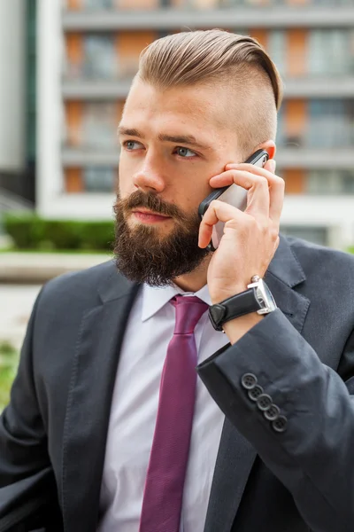 Mladé vousatých podnikatel pomocí mobilního telefonu mimo kancelář. — Stock fotografie