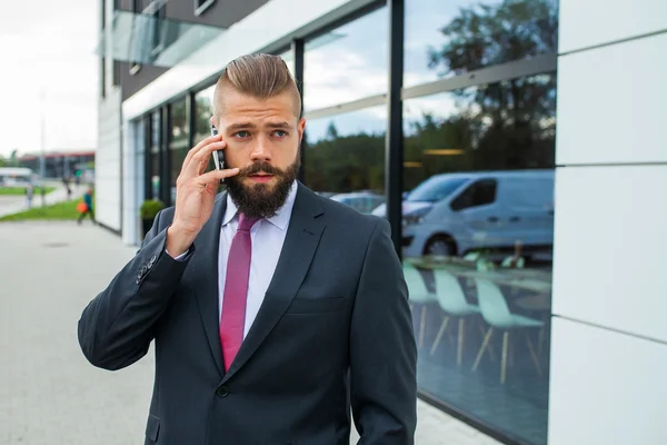 Mladé vousatých podnikatel pomocí mobilního telefonu mimo kancelář. — Stock fotografie