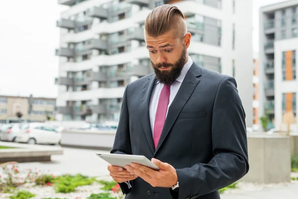 Jonge, bebaarde zakenman met zijn tablet-pc. Hij is verbaasd. — Stockfoto