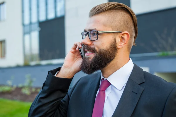 Young bearded businessman wearing eyeglasses using mobile phone — Stock Photo, Image