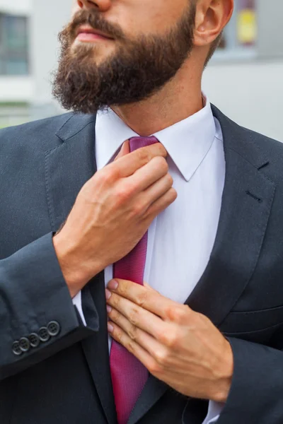 Young attractive businessman ajusting his tie. Outdoor photo. — Stock Photo, Image