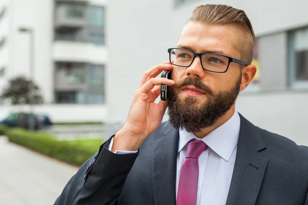 Joven hombre de negocios barbudo con anteojos usando teléfono móvil — Foto de Stock