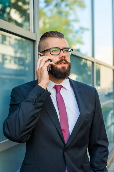 Young bearded businessman wearing eyeglasses using mobile phone — Stock Photo, Image