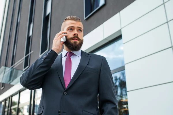 Jeune homme d'affaires barbu utilisant un téléphone portable à l'extérieur du bureau . — Photo