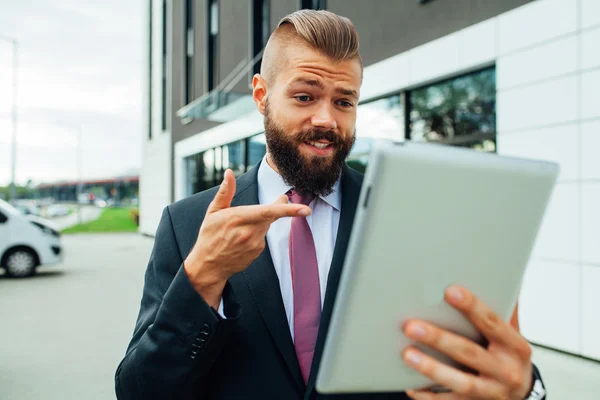Jonge, bebaarde zakenman met zijn tablet-pc. Hij is verbaasd. — Stockfoto