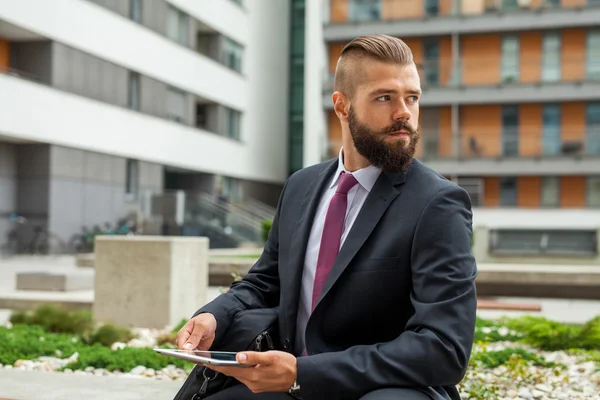 Young bearded businessman sitting on a bench and using tablet pc — Stock Photo, Image