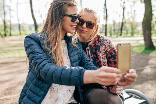 Zwei Mädchen sitzen auf dem Bech im Park und machen Selfie. — Stockfoto