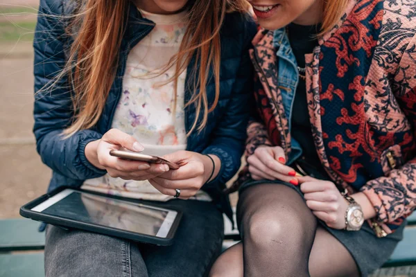 Две девушки сидят в парке с планшетным ПК и мобильным телефоном. C — стоковое фото