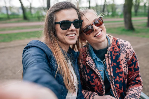 Dvou dívka sedící na bech v parku a přijetí selfie. — Stock fotografie