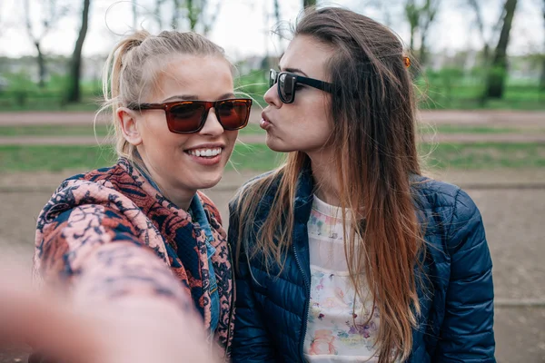 Zwei Mädchen sitzen auf dem Bech im Park und machen Selfie. — Stockfoto