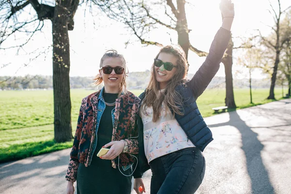 Zwei Mädchen, die im Park spazieren und Musik hören. — Stockfoto