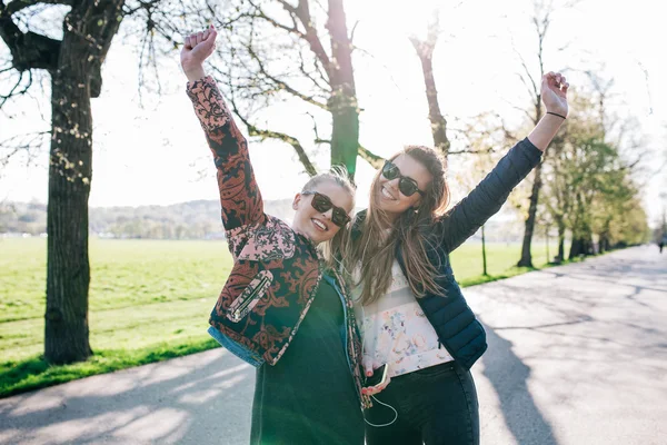 Zwei Mädchen hören Musik im Park. Hände hoch. — Stockfoto