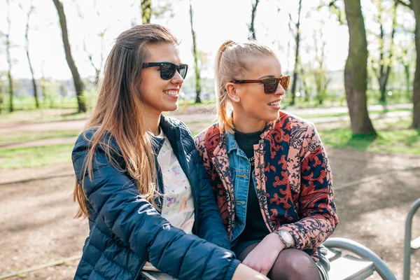 Zwei Mädchen, die auf der Bucht im Park sitzen. die schauen auf som — Stockfoto