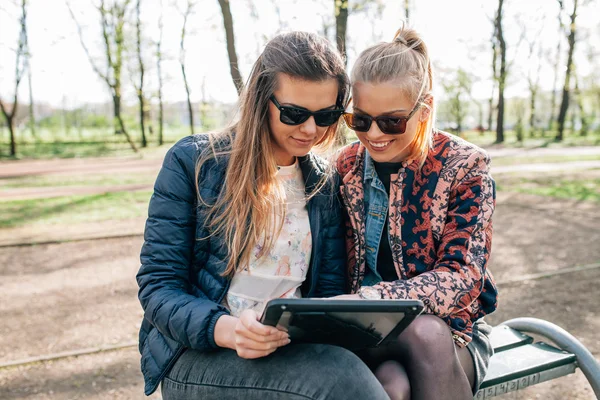 Due ragazze sedute sul bech nel parco e utilizzando tablet pc . — Foto Stock