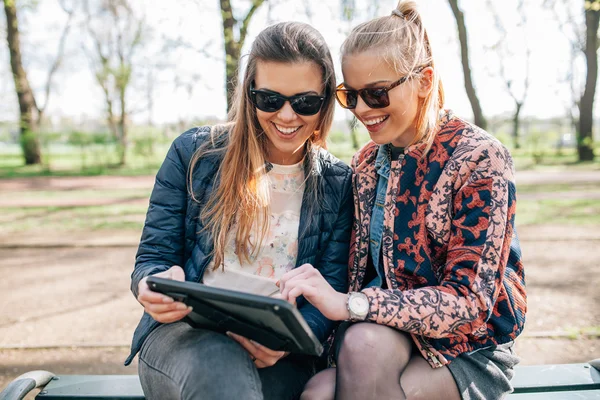 Dvě dívky sedící na bech v parku a použití počítače tablet pc. — Stock fotografie