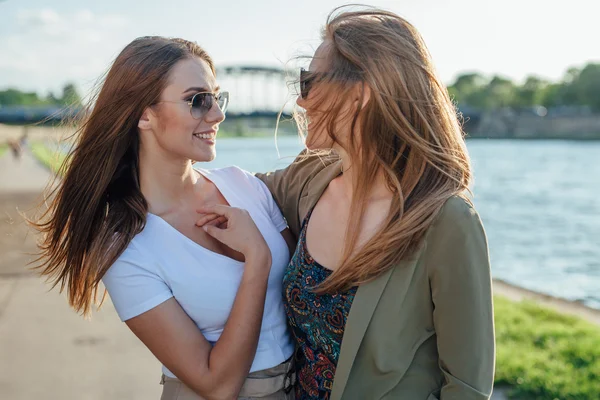 Zwei glückliche junge Mädchen, die am Fluss stehen und reden. — Stockfoto