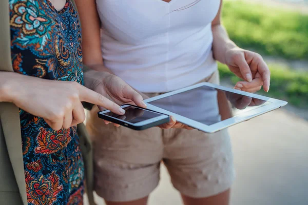 Dos chicas jóvenes de pie junto al río y el uso de tableta pc . — Foto de Stock