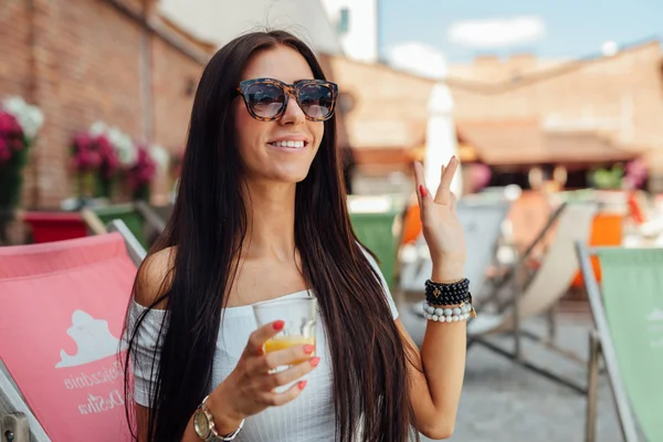 Ung flicka med organge juice vinkar till någon. — Stockfoto