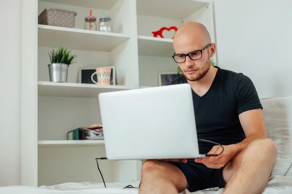 Młody człowiek jest przy użyciu komputera typu tablet i siedzi na łóżku. Podłoże do domu — Zdjęcie stockowe