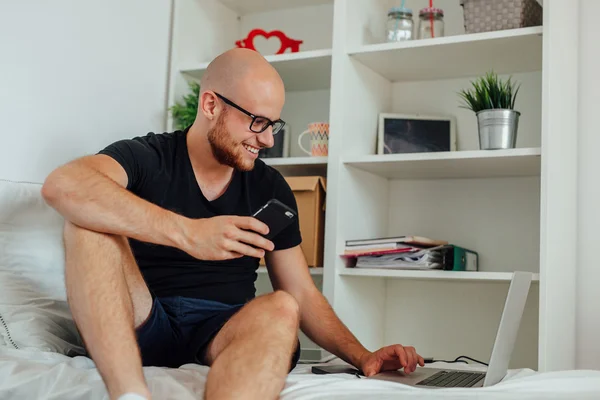 El hombre joven está utilizando la PC portátil y la celebración de móviles. Respaldo casero —  Fotos de Stock