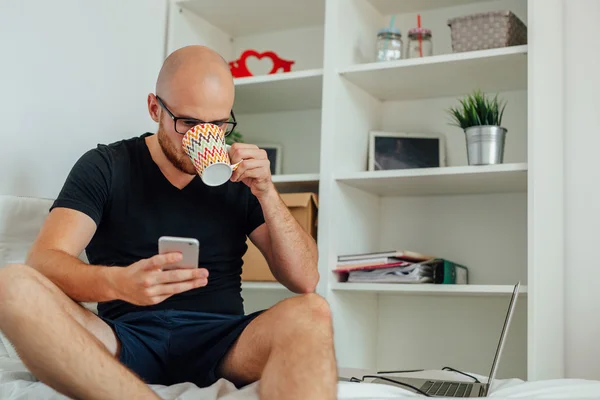 Joven está bebiendo algo de la taza y usando el móvil . —  Fotos de Stock