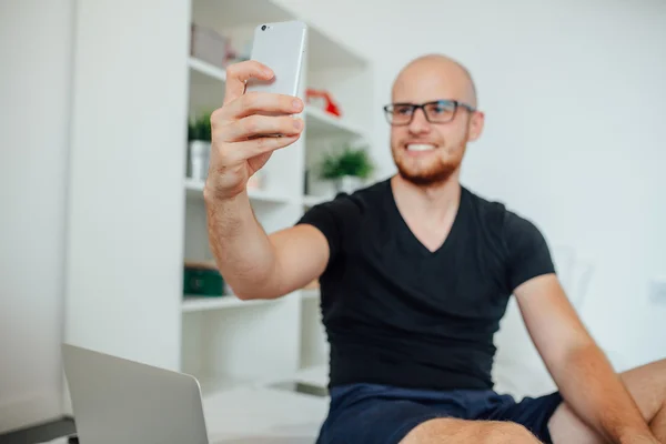 O jovem está a tirar uma selfie enquanto está sentado na cama. Home backgrou — Fotografia de Stock