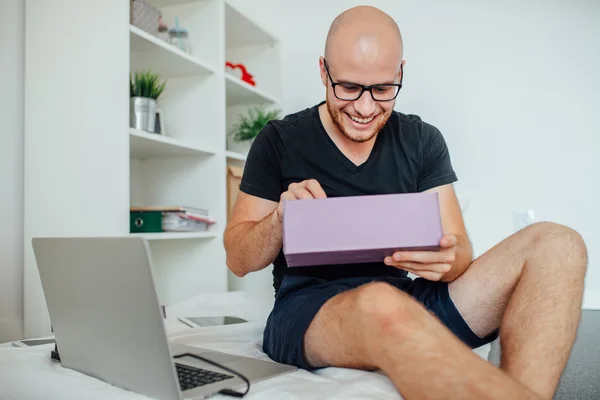 El joven disfruta abriendo cajas y sentándose en la cama. Respaldo casero —  Fotos de Stock