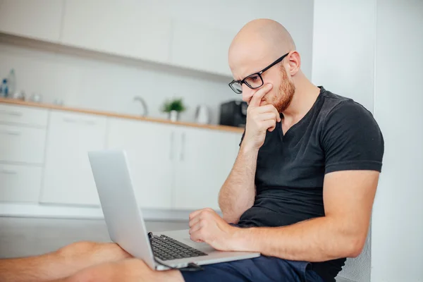 Młody człowiek jest za pomocą jego pc laptop. Kuchnia tło — Zdjęcie stockowe