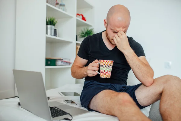 Ung man gnugga ögonen och hålla en mugg. Hem bakgrund Stockbild