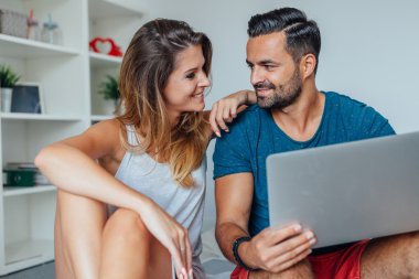 Genç çift yatakta oturuyor ve dizüstü pc Online kullanarak